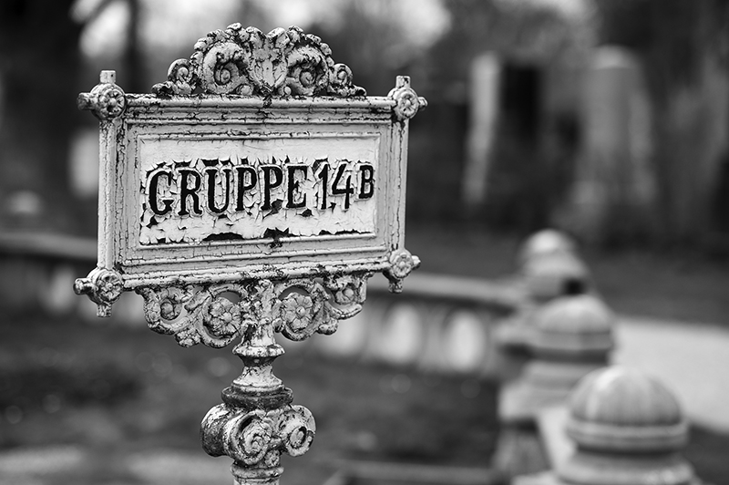 Schwarzweiß Aufnahme eines verwitterten Gusseisen-Schildes mit der Aufschrift "Gruppe 14B", der Hintergrund ist unscharf