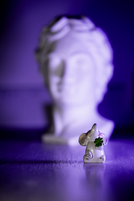 Kleine Figur eines Elefanten, dahinter eine unscharfe, weiße Büste, der Großteil des Bildes ist in Blau gehalten