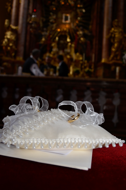 Ein kleines, weißes Polster mit zwei Ringen, die von einer weißen Masche gehalten werden - im Hintergrund ein barocker Altar