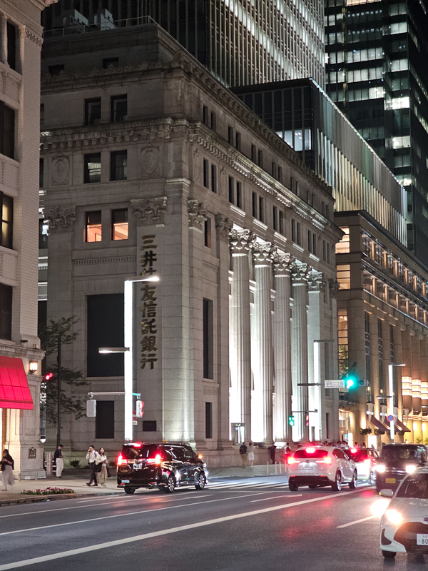 Nachtszene einer Straße in Tokyo mit modernen Häusern im Hintergrund, im Vordergrund ein älteres Haus mit einer japanischen Aufschrift
